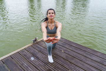 Fototapeta na wymiar latin woman in sportswear stretching in river. Horizontal view of fitness woman training outdoors.
