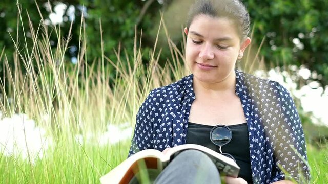 Mujer cauc&aacute;sica leyendo un libro en el campo a la orilla de un lago