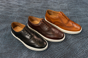 Formal golf wingtip sneakers on a blue textured leather background. The mens fashion footwear has a white outsole and is a fancy sneaker.