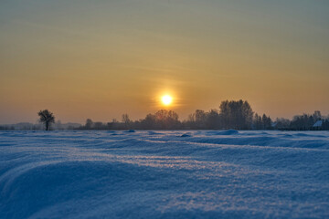 A snowy frozen field in the rays of the setting winter sun