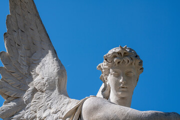 Angel with wings against blue sky. Ancient statue.