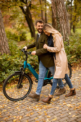 Fototapeta na wymiar Young couple in the autumn park with electrical bicycle