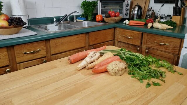 Home cooking - Panning left to right of vegetables like carrot, rooted parsley, celery and parsnip being ready on kitchen table to be cleaned for cooking.