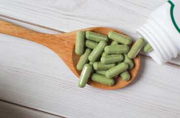 Andrographis paniculata capsule in wooden spoon on wooden background., Herbal extract medicine tablets pills.