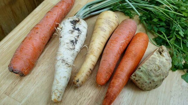 Home cooking - High angle view and panning left to right of vegetables like carrot, rooted parsley, celery and parsnip being ready to be cleaned for cooking.