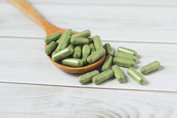 Andrographis paniculata capsule in wooden spoon on wooden background., Herbal extract medicine tablets pills.