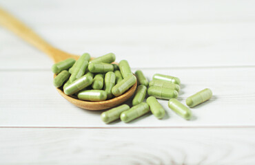 Andrographis paniculata capsule in wooden spoon on wooden background., Herbal extract medicine tablets pills.