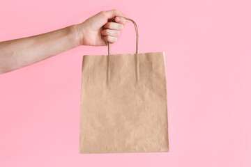 A man holds a craft package on a colored background. Blank space on a brown paper bag. Place for...