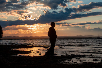 Mountain lake at sunset. The yacht sways on the waves. Silhouette of a girl at sunset
