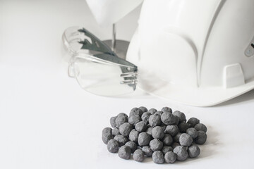 Iron ore pellets on a white background, with a white safety helmet and goggles in the background....