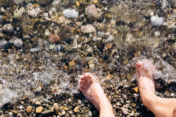 Legs of a man on the shore of a stone beach of the sea. Space for copying text