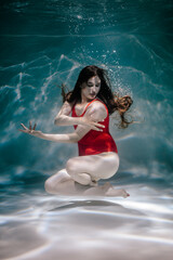 A girl swims under the water in a red bodysuit