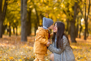 Young beautiful mother spends time on a walk with her beloved little son in the autumn park