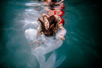 A girl swims underwater in a red bodysuit with a white fabric