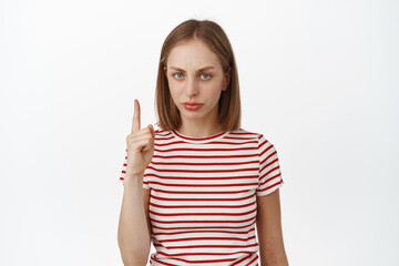Upset blond girl pointing finger up, frowning displeased, dislike smth, express her negative...