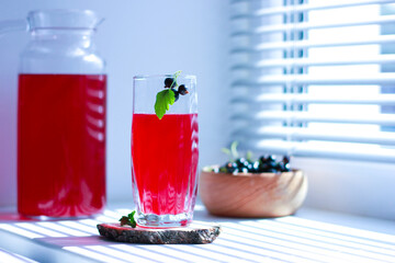 black currant juice with a glass glass on the window in the shade of the blinds, summer soft drinks, healthy food