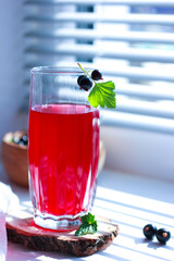 black currant juice with a glass glass on the window in the shade of the blinds, berries, summer soft drinks, healthy food