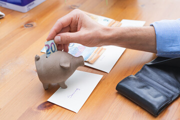 Hand stuffing a bill into a piggy bank for savings. Copy space.