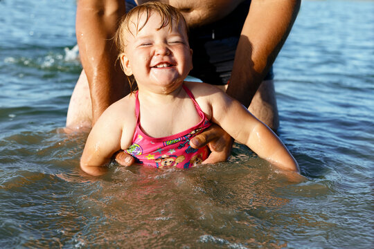 The smiling girl in pink swimsuit swims holding daddy's hands