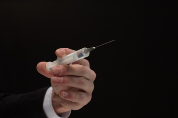 Human hand holding syringe with vaccine on black background