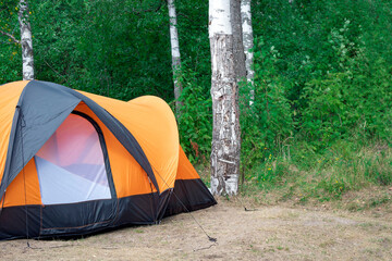 Orange big camping tent on background green forest with birch trunks. Travel around Russia, life in tent camp, outdoor recreation. Concept of holiday away from noisy polluted cities in nature.