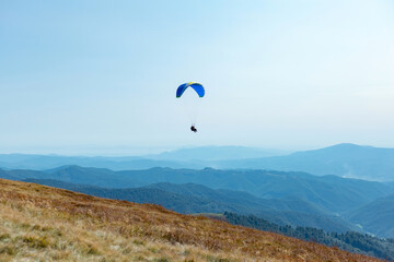 Paragliding over mountains with parachute. Paragliding behind blue sky hills range landscape. Active tourist sport People fly using Parachute.