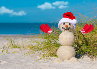 Snowman on the beach. Sandy Christmas snowman in red Santa hat and mittens or gloves. Smiley...