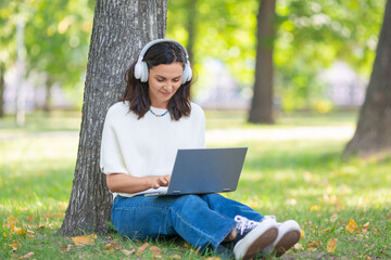 Photo of a middle aged woman with laptop in city park. Online working or online education concept.