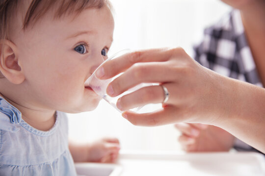 Infant baby girl drinks water from baby cup holded by her mother