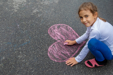 The child draws with chalk on the asphalt. Selective focus.