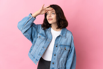 Teenager Ukrainian girl isolated on pink background looking far away with hand to look something