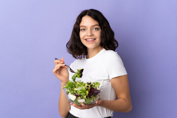 Teenager Ukrainian girl isolated on purple background holding a bowl of salad with happy expression