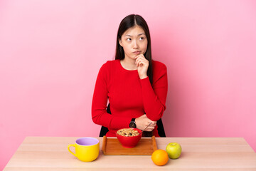 Young Chinese girl  having breakfast in a table having doubts and thinking