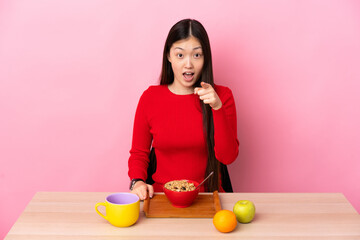 Young Chinese girl  having breakfast in a table surprised and pointing front