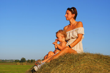 Little boy with mom on a haystack. Mom with baby on a background of blue sky. Mom with a small child on a pile of hay