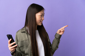 Young Chinese girl using mobile phone over isolated purple background pointing to the side to present a product