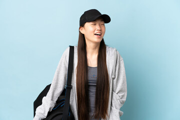 Young sport Chinese  woman with sport bag over isolated blue background laughing