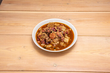 Super plate of tripe a la Madrid with chorizo slices and ham cubes with black pepper on a wooden table.