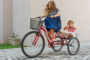 Criança transporta irmã em triciclo com alegria