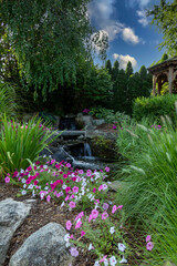 Landscape architecture with pink flowers and ornamental grasses for summer garden with waterfall