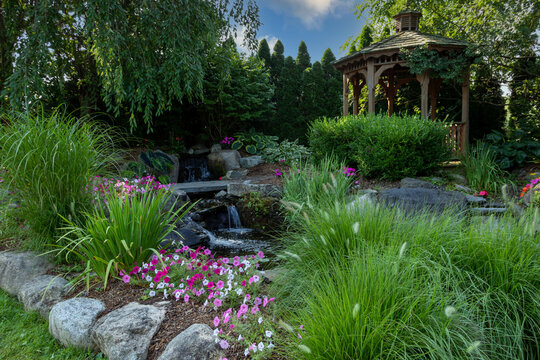 Landscape architecture with pink flowers and ornamental grasses for summer garden with waterfall