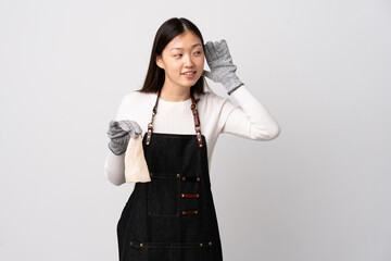 Chinese fishmonger wearing an apron and holding a raw fish over isolated white background listening to something by putting hand on the ear