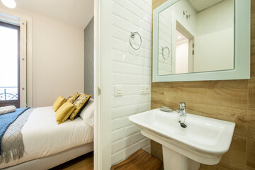 Toilet with white sink and mirror next to a king size bed in a modern vacation rental apartment