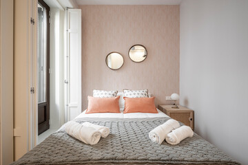 King bed in a vacation rental apartment room with cushions and orange wallpaper and a large view to the street