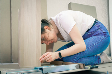 Millennial woman doing DIY putting together self-assembly wooden furniture at living room