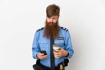 Redhead police man isolated on white background holding coffee to take away and a mobile