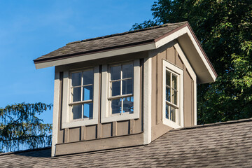 Rustic decorative cupola a hollow frame that protrudes up from the roof of a barn building with double windows on all sides, blue sky background 