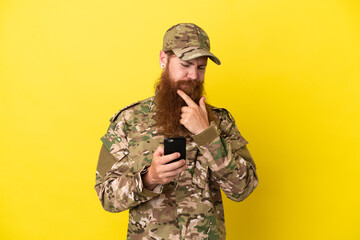 Military Redhead man over isolated on yellow background thinking and sending a message