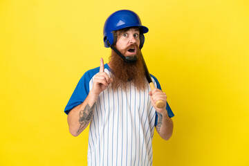 Redhead baseball player man with helmet and bat isolated on yellow background thinking an idea pointing the finger up