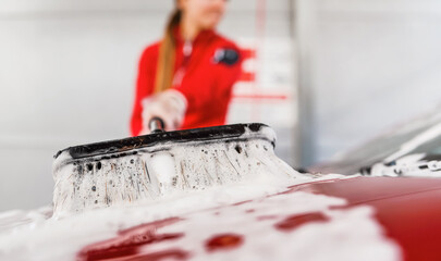 Young woman cleaning her car in self serve carwash. Closeup detail on white soap foam and brush...
